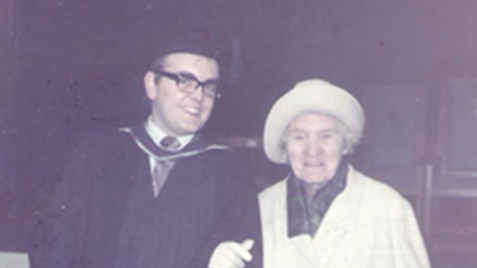 Barry in his graduation gown and hat with his grandmother. They are smiling together.